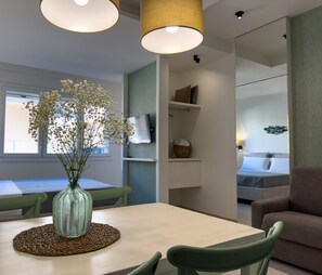 A modern interior with a dining area featuring a table, chairs, and a vase with flowers. There is a sofa and a bed in the adjacent room.