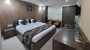 Une chambre à coucher comprenant un lit, des tables de chevet, un bureau, une chaise, un ventilateur de plafond et un téléviseur fixé au mur.