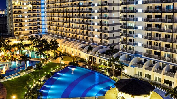 A multi-story hotel with a swimming pool and palm trees. - Ardent 1BR Condo Front of Mall of Asia Pasay City (Pasay)