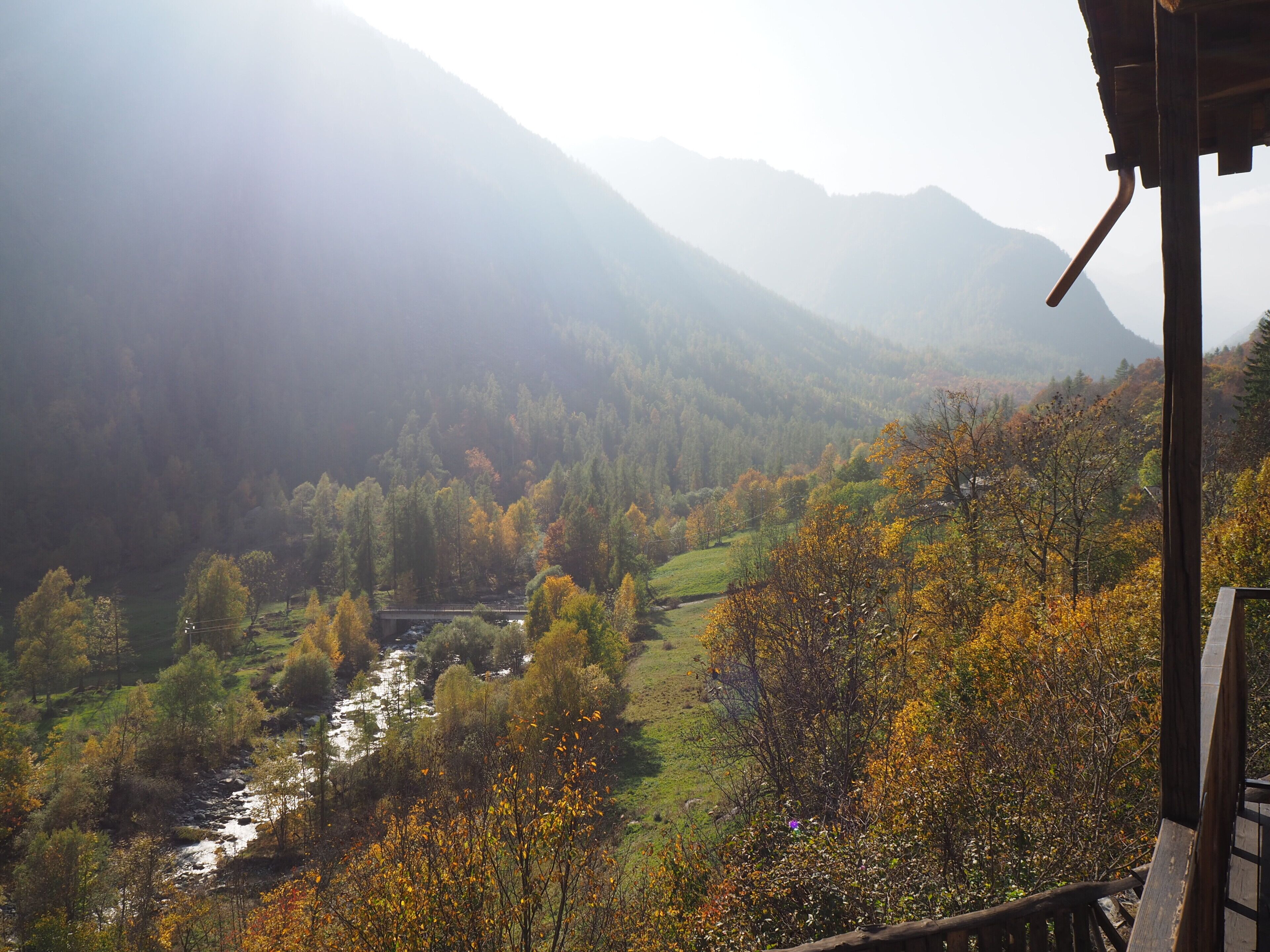A mountainous landscape with a river, trees in autumn colors, and a wooden structure.