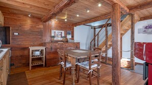 A wooden interior with a dining table, chairs, a kitchen area, and a staircase.