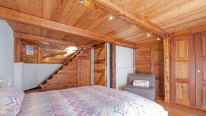 A wooden interior with a bed, a chair, and a staircase.