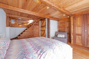 A wooden interior with a bed, a chair, and a staircase.