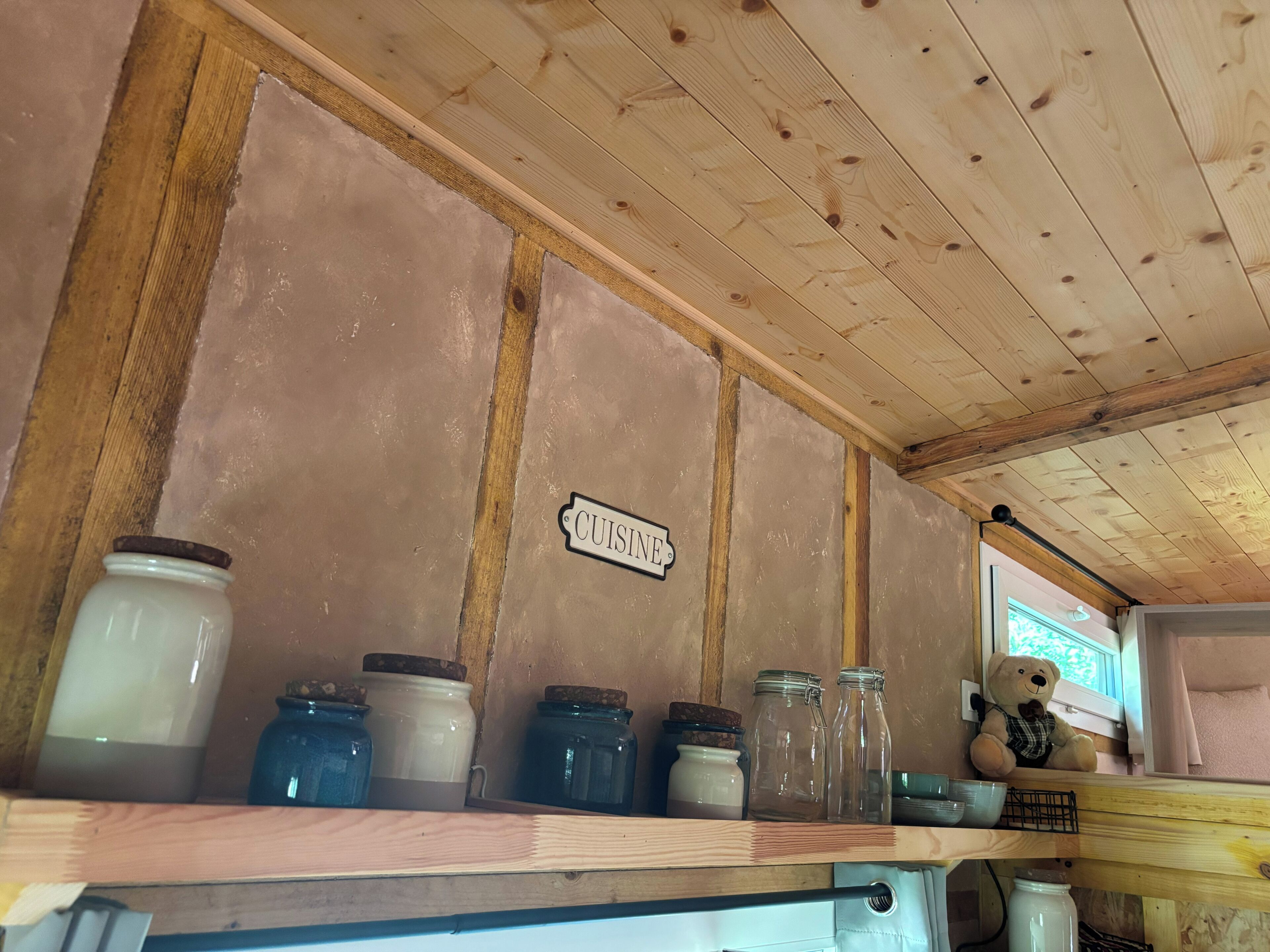 Un angolo cottura con soffitto in legno, un cartello con scritto 'CUISINE' e diversi barattoli su uno scaffale.