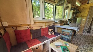 A cozy room with a bench, a table with books, and a view of the outdoors. - Hempcrete Tiny House (Malbrans)