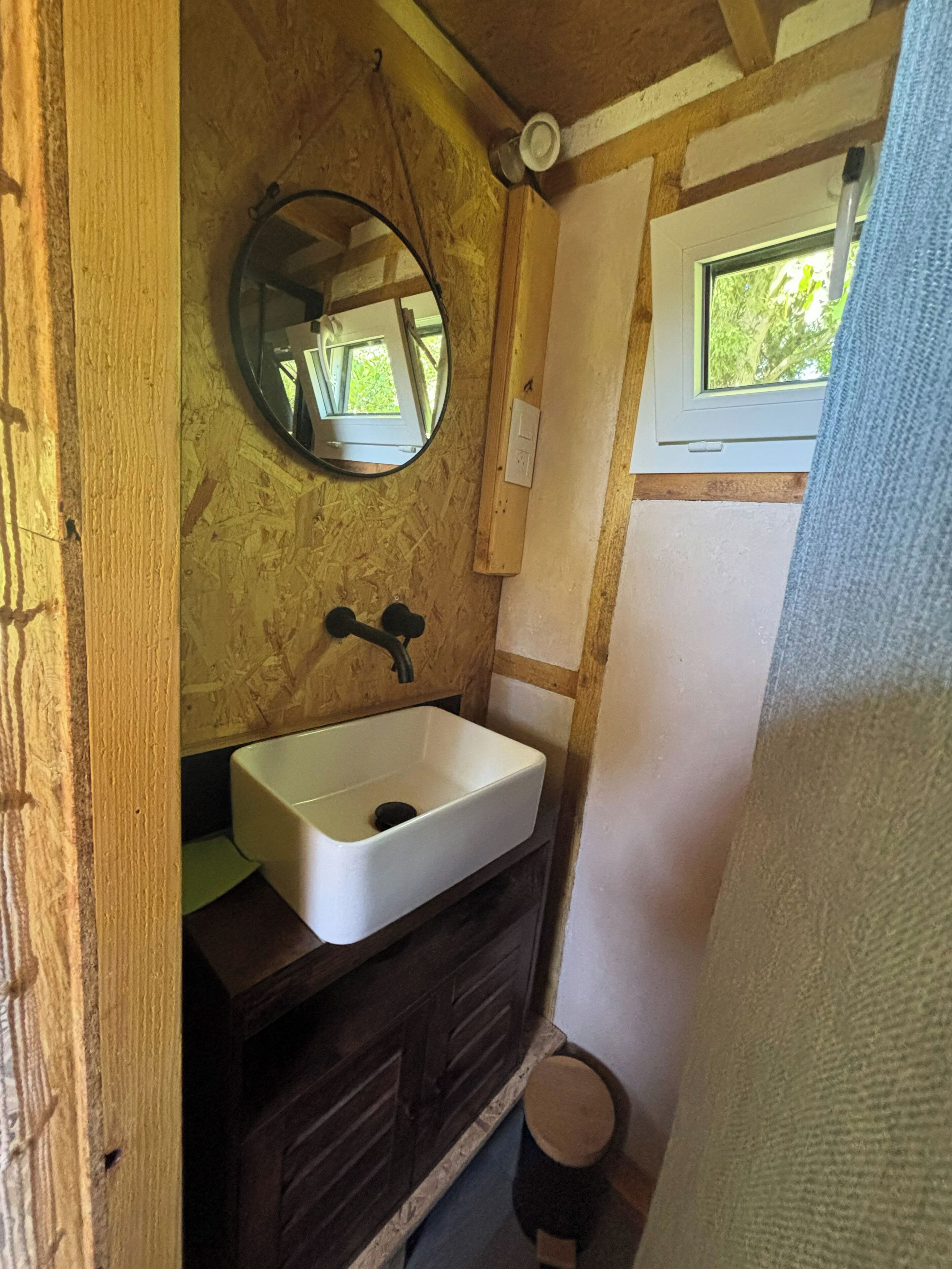 A compact bathroom with a white sink, wooden vanity, and a mirror.
