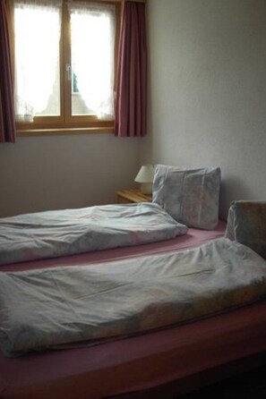 A room with two single beds, a nightstand with a lamp, and a window with curtains. - Claveniev , (Disentis/Mustér), 1036 by Interhome (Disentis)