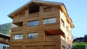 A multi-story wooden building with balconies, large windows, and a mountainous backdrop. - Tgèsa Muntaniala Stamm, (Sedrun), 198.02 by Interhome (Sedrun)