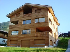 A multi-story wooden building with balconies, large windows, and a mountainous backdrop. - Tgèsa Muntaniala Stamm, (Sedrun), 198.02 by Interhome (Sedrun)