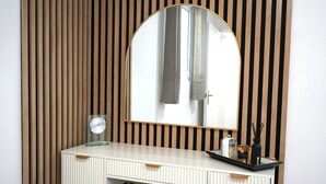 A white vanity with a mirror, a clock, and a tray with a bottle and a candle.