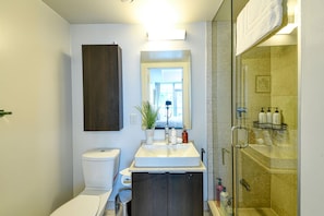 Un baño moderno con un lavabo blanco, muebles bajos de madera oscura, una ducha con cerramiento de vidrio y un ventanal.