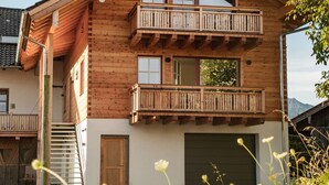 A two-story wooden house with a balcony on the upper floor, a garage, and a staircase leading to the entrance. - Henriette Vacation Rental (Teisendorf)