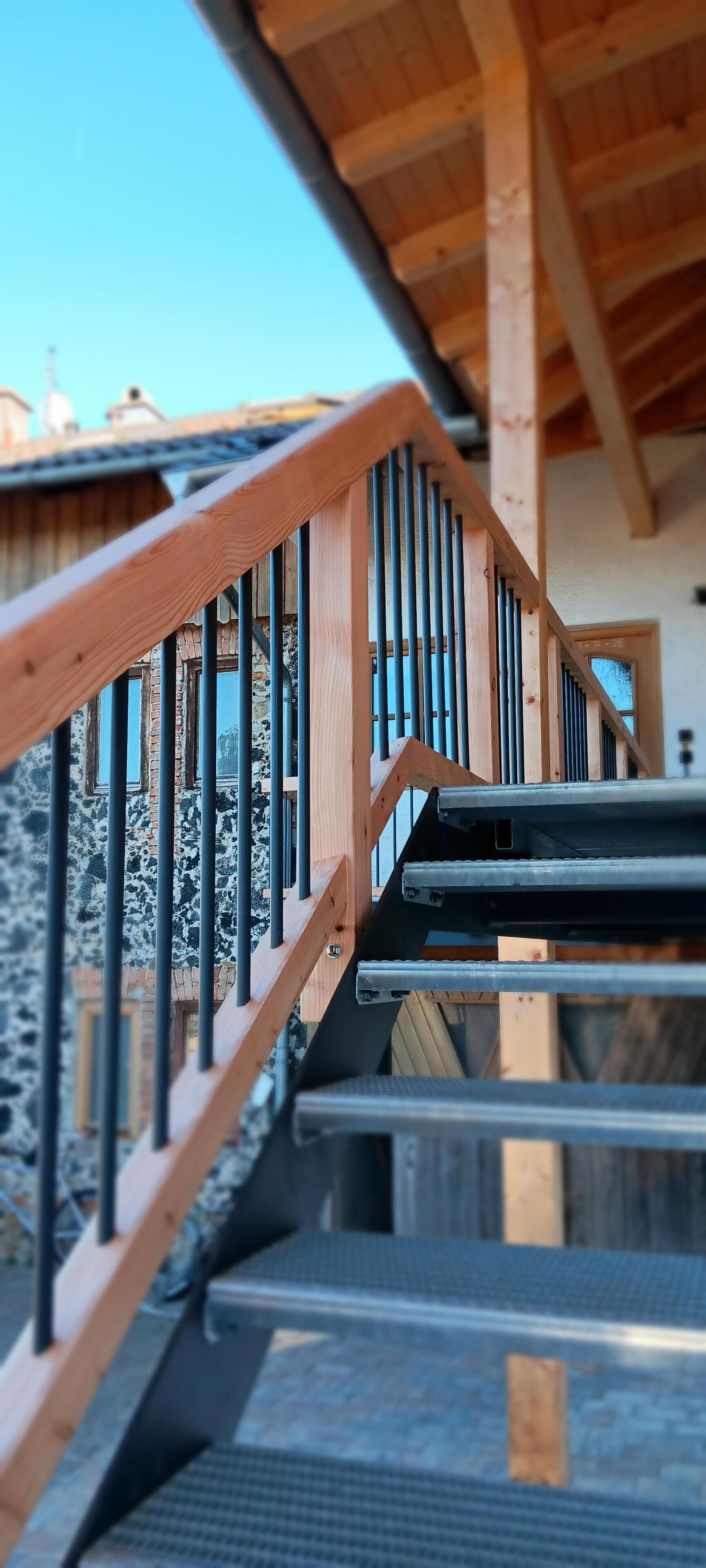 Eine Holztreppe mit Metallgeländern, die zu einer oberen Ebene führt.