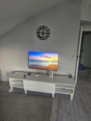 A room with a flat-screen TV on a white entertainment unit, a wall clock, and a door leading to another room. - Gorgeous apartment close to the sea with private beach (Antalya)