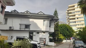 Ein Wohngebäude mit Balkon, geparkten Fahrzeugen und einem benachbarten Hochhaus.