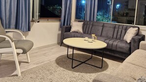 Ein Wohnzimmer mit einer Couch, einem runden Couchtisch, einem Sessel und einem großen Fenster mit Vorhängen.