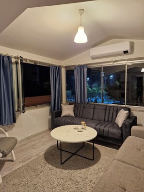 A living room with a sofa, a coffee table, and a hanging light fixture. - Gorgeous apartment close to the sea with private beach (Antalya)
