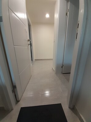 A hallway with white walls and doors, a tiled floor, and a black mat at the entrance. - Gorgeous apartment close to the sea with private beach (Antalya)
