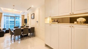 A modern kitchen with white cabinetry, a dining area with a table and chairs, and a view of a building through large windows. - Tranquil 2-bedroom condo with AC in Thành phố Hồ Chí Minh (Thành phố Hồ Chí Minh)