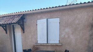 Un patio con una mesa, sillas, una puerta y una ventana con contraventanas.