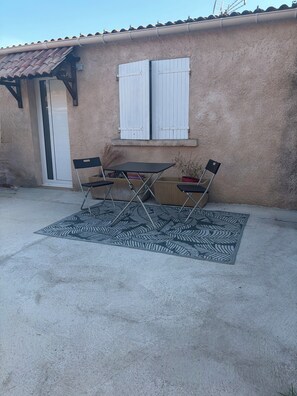 Eine Terrasse mit Tisch, Stühlen, einer Tür und einem Fenster mit Rollläden.