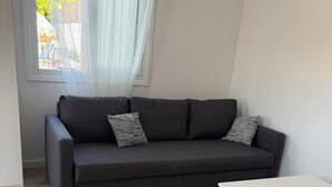 Una sala de estar moderna con un sofá gris, dos cojines estampados, una mesa de centro blanca y una ventana con cortinas de gasa.