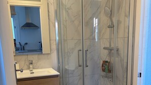 Un baño con ducha de vidrio, lavamanos con espejo y un inodoro.
