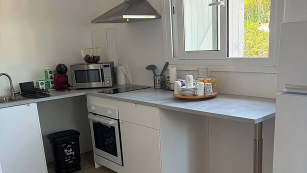 Una cocina moderna con armarios blancos, una campana extractora de acero inoxidable, microondas, cafetera y ventana con vistas a zonas verdes.