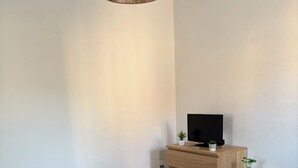 Una habitación minimalista con un banco blanco, un aparador de madera y un televisor encima.