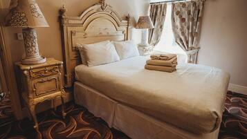 A hotel room with a large bed, a nightstand with a lamp, a headboard, and a window with curtains.