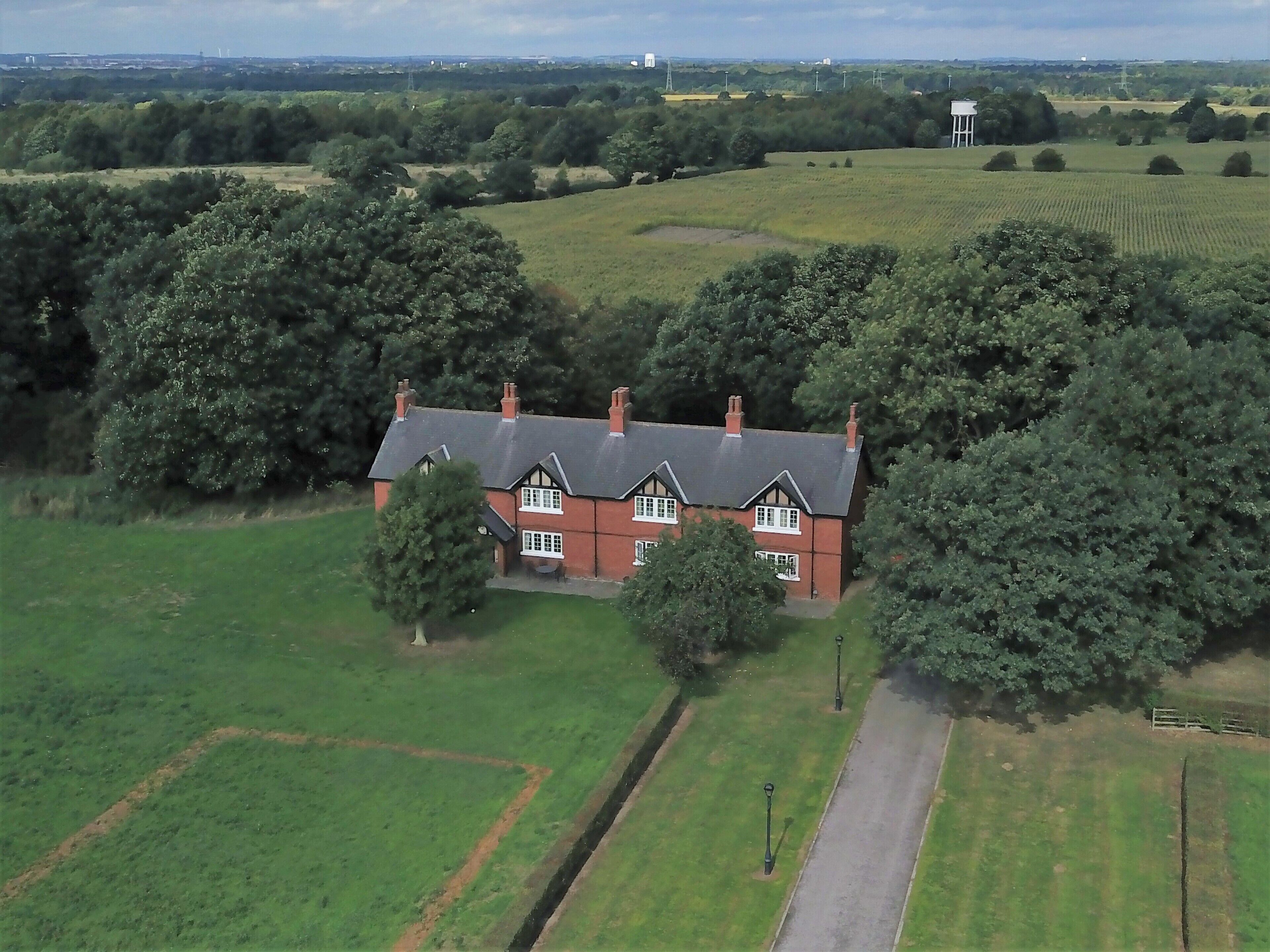 A large house with a sloped roof, surrounded by green fields and trees.