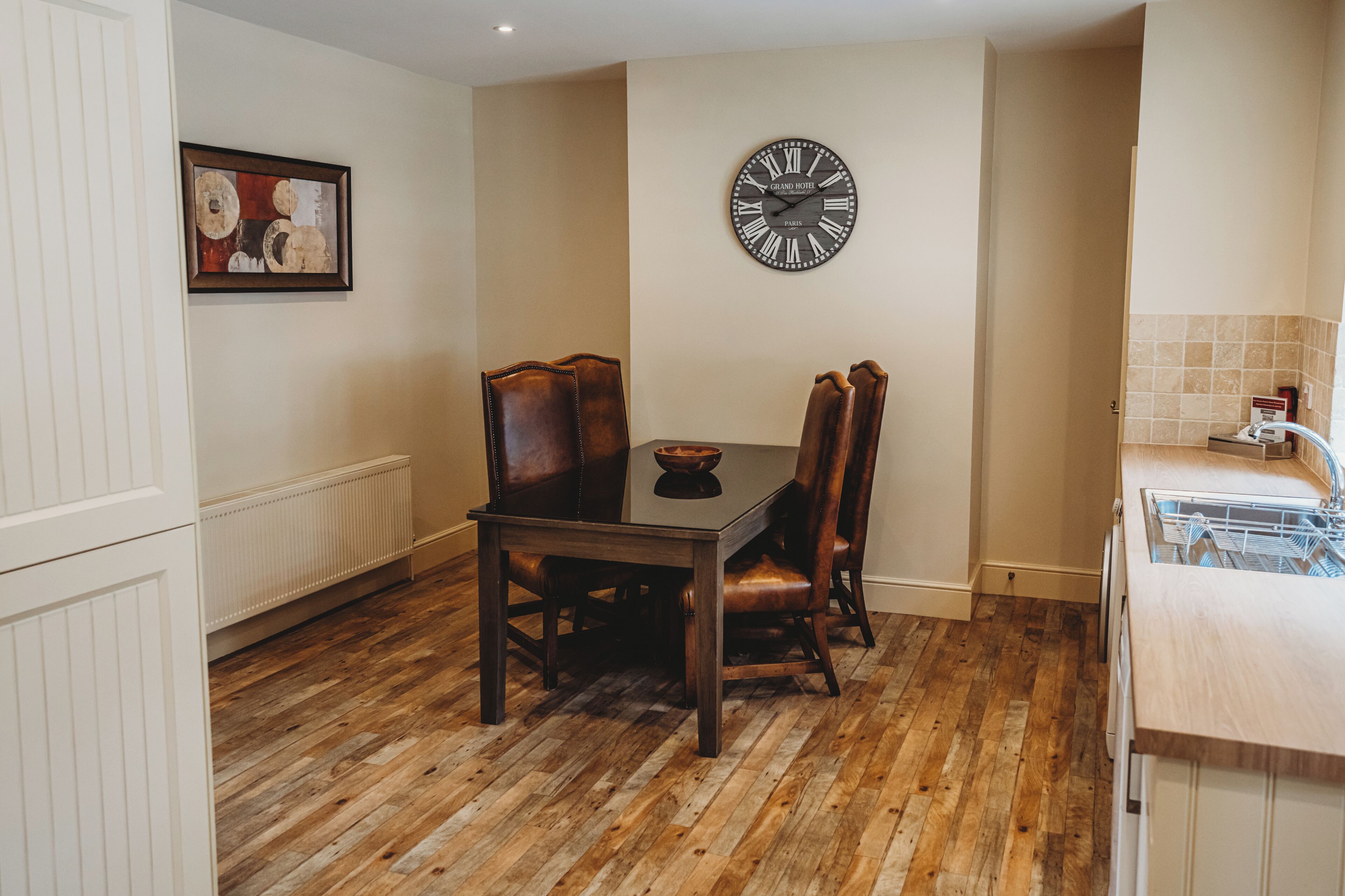 A dining area with a wooden table and chairs, a wall clock, and a radiator.