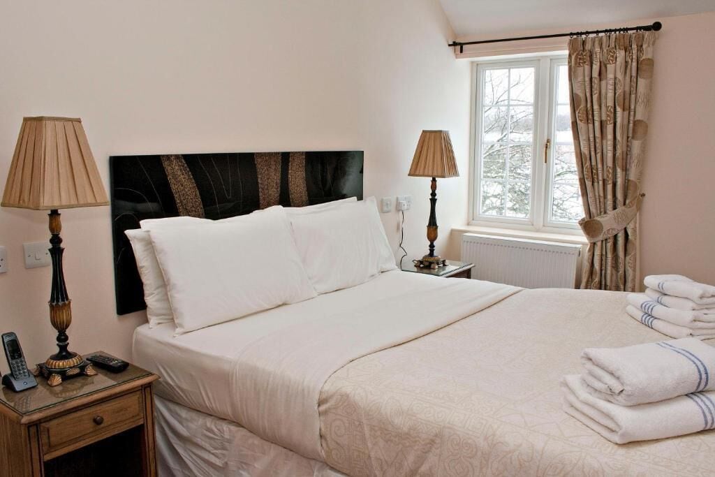 A hotel room with a bed, bedside lamps, a window with curtains, and a radiator.