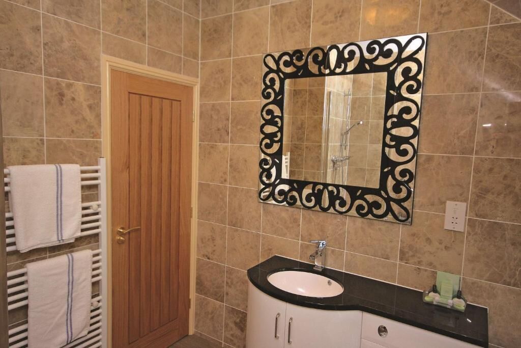 Un bagno con una porta in legno, un lavandino bianco su un piano di lavoro nero e uno specchio decorativo con cornice nera.