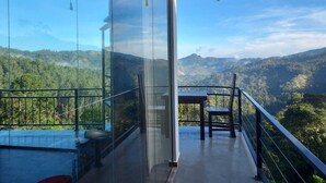 Een balkon met glazen balustrade, uitzicht op een bebost berglandschap.