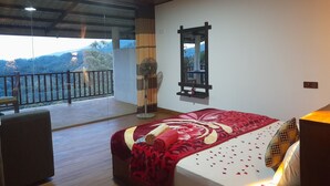 Een slaapkamer met een groot bed, een ventilator, een spiegel en een balkon met uitzicht op het landschap.