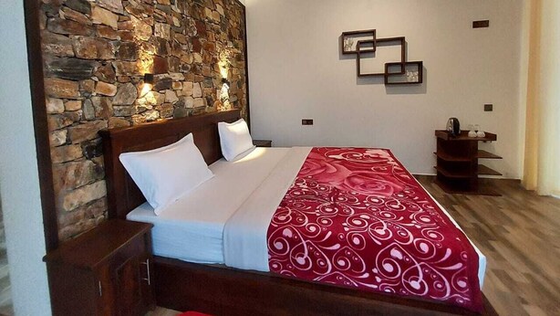 Een slaapkamer met een stenen muur, een bed met witte beddengoed, een rode, gestreepte plaid en een nachtkastje.