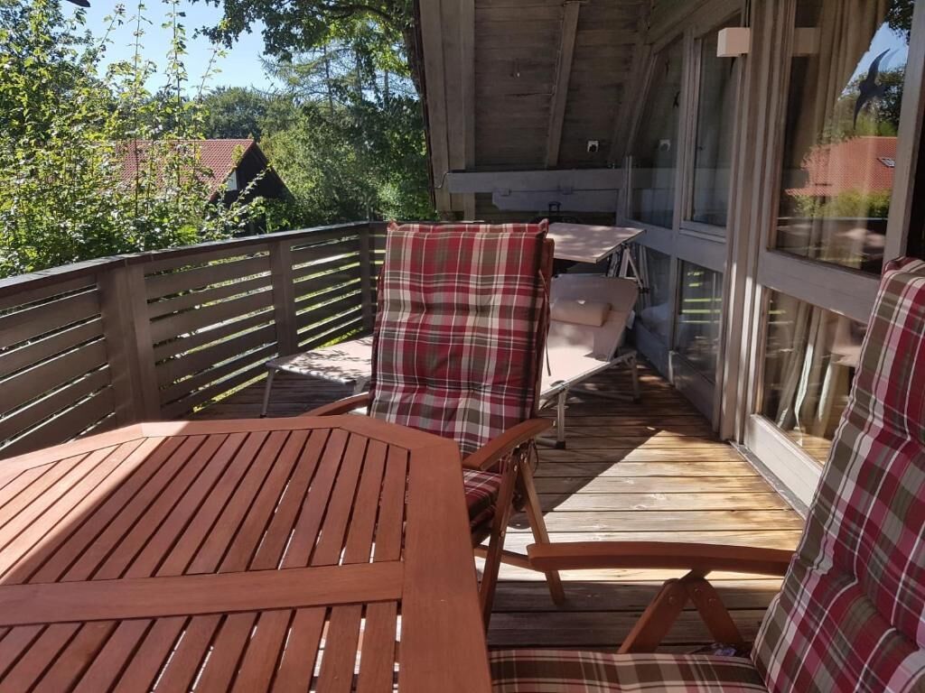 A wooden deck with a table and chairs, a glass door, and a view of trees and buildings.