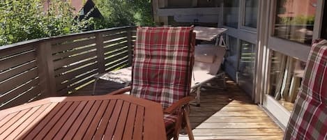 A wooden deck with a table and chairs, a glass door, and a view of trees and buildings.