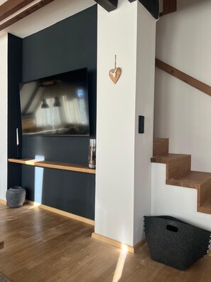 Ein modernes Wohnzimmer mit Flachbildfernseher, einer Holztreppe und einer herzförmigen Dekoration an der Wand.