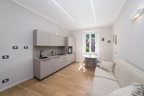 Eine moderne Küche mit eingebauten Geräten, ein Essbereich mit rundem Tisch und ein beiges Sofa.