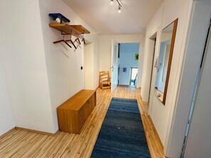 Un pasillo con suelo de madera, alfombra azul, un banco de madera, una silla y un espejo en la pared.