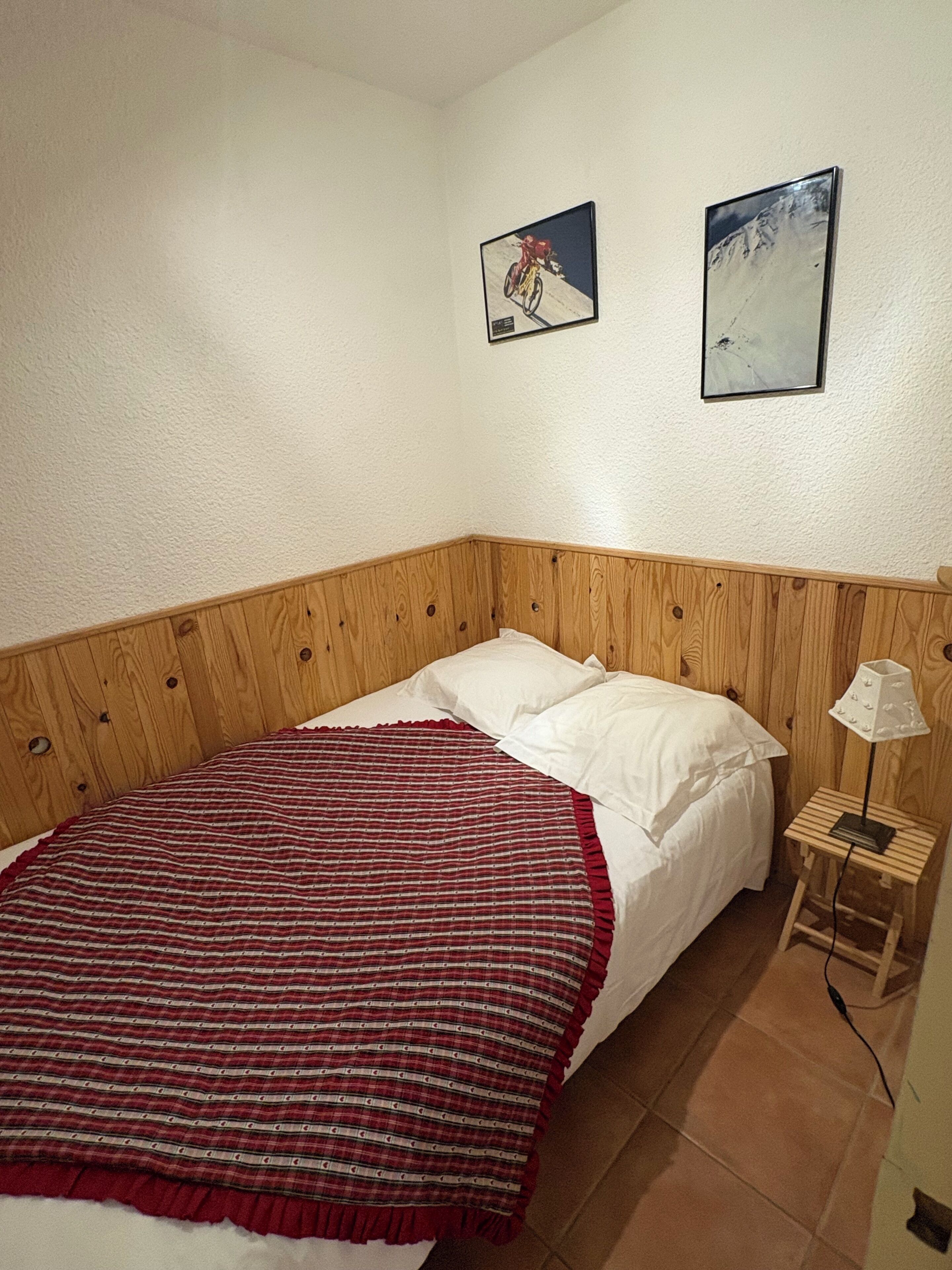 Ein Schlafzimmer mit einem Holz-Kopfteil, einem Bett mit weißer Bettwäsche, einer rot-weißen Streifendecke und zwei gerahmten Bildern an der Wand.