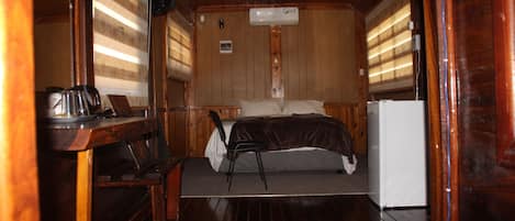 Una cabaña pequeña con cama, una mesita con hervidor y refrigerador.