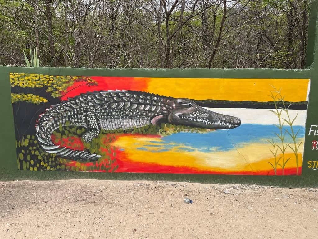 A mural of a crocodile on a wall with trees in the background.