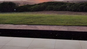 A sunset view from a paved terrace with a grassy field and distant hills.