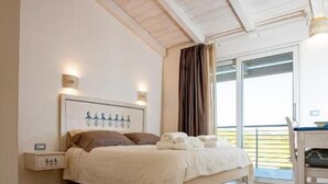 A bedroom with a bed, bedside table, and a view of the outdoors.