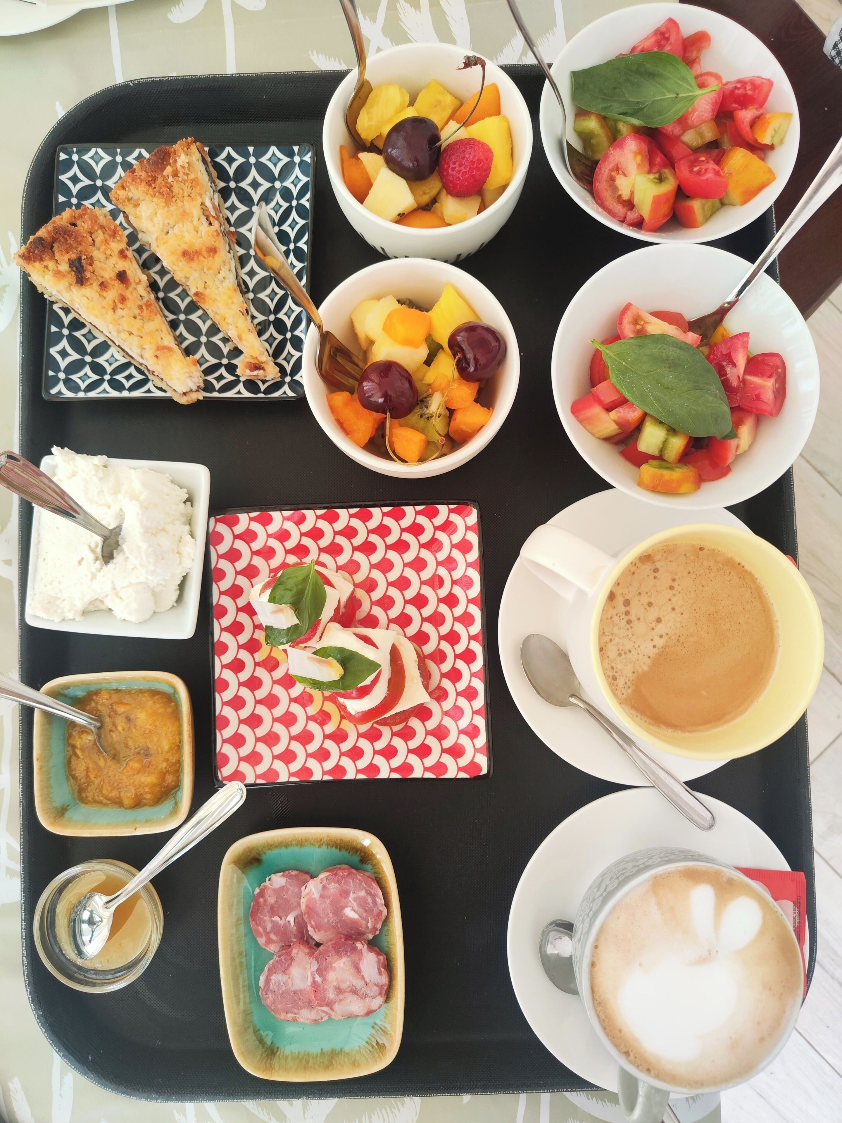 A tray with various food items including toast, fruit, a bowl of rice, a plate of meat, a cup of coffee, and a small bowl of sauce.