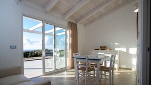 A modern interior with a dining area, a sofa, and a view through large glass doors.