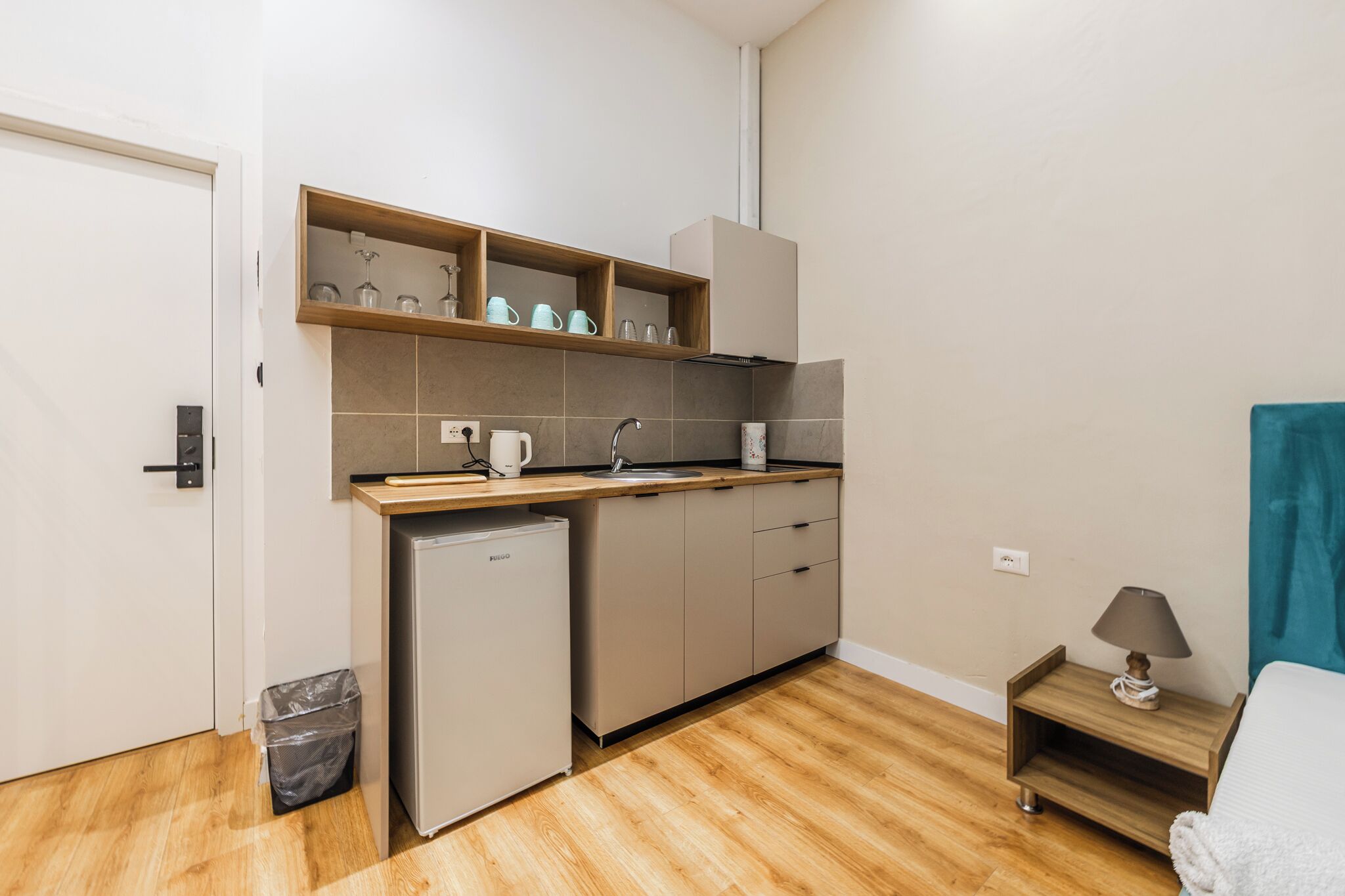 Eine kompakte Küchenzeile mit Kühlschrank, Spüle und einer Arbeitsplatte mit Stauraumregalen.